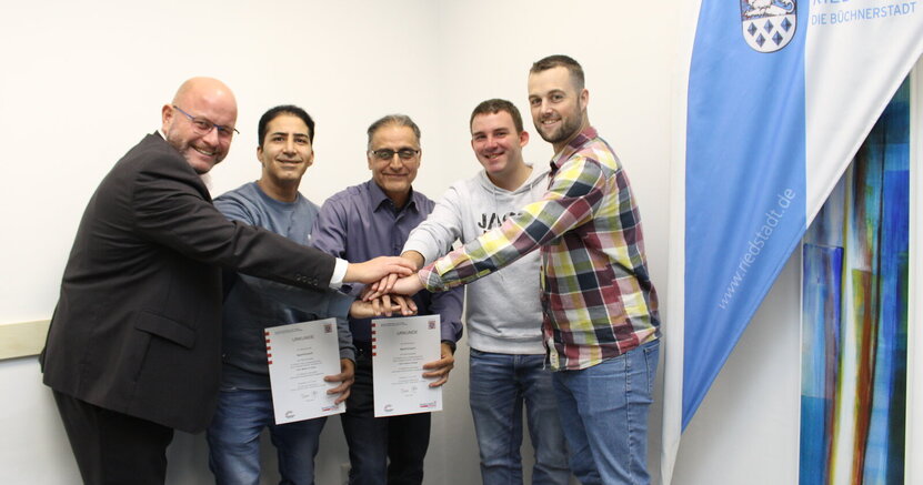 Bürgermeister Marcus Kretschmann, Maher Al Gnem, Samer Chawaf, Tobias Menke und Fachbereichsleiter Rick Hölzer (v.li.) mit den Urkunden. Bürgermeister Marcus Kretschmann, Maher Al Gnem, Samer Chawaf, Tobias Menke und Fachbereichsleiter Rick Hölzer (v.li.) legen ihre Hände übereinander.
