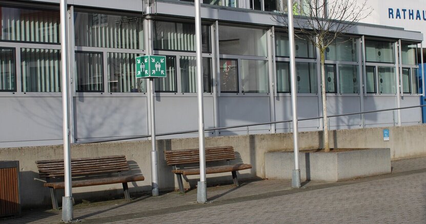 Sitzbänke stehen unter anderem auch vor dem Riedstädter Rathaus. Zu sehen ist das Riedstädter Rathaus von außen. Davor stehen zwischen Fahnenmasten zwei Sitzbänke.