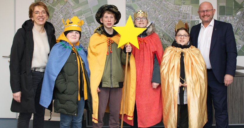 Die Sternsinger mit Dagmar Bahrenberg und Bürgermeister Marcus Kretschmann. Vier Kinder sind als Sternsinger verkleidet. Eines hat einen Stab mit Stern in der Hand. Neben ihnen stehen ihre Betreuerin Dagmar Bahrenberg und Bürgermeister Marcus Kretschmann.