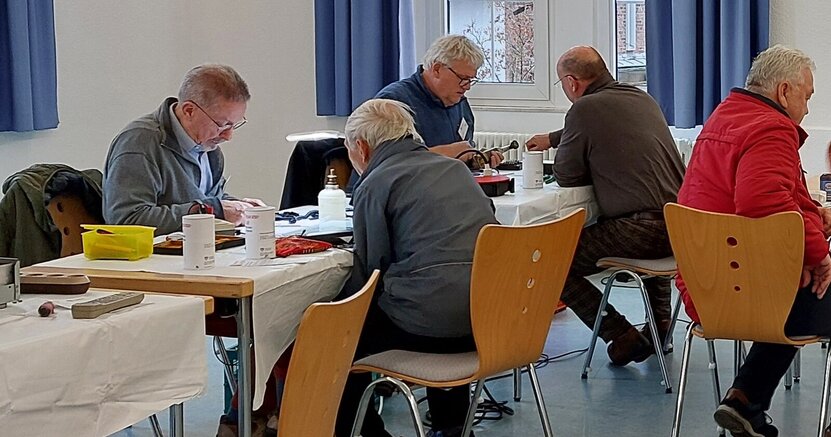 Gemeinschaftlich gewerkelt wird beim Reparatur-Café im alten Rathaus Crumstadt. Männer sitzen sich an Tischen gegenüber und reparieren Geräte.