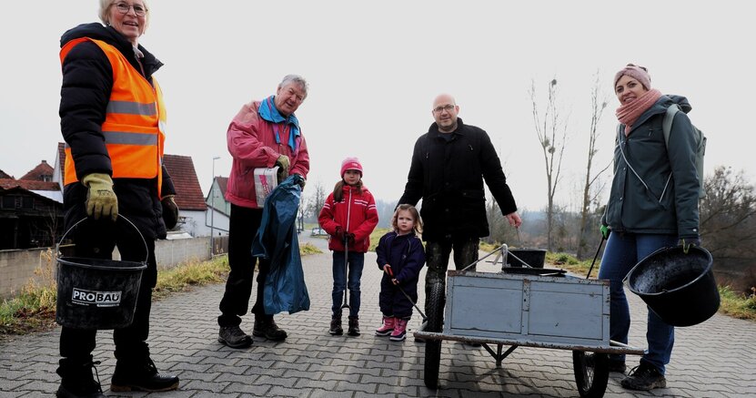 Auch in Erfelden wurde im letzten Jahr eifrig von Groß und Klein gesammelt. Erwachsene und Kinder stehen auf dem Damm in Erfelden. Sie haben Mülltüten, Eimer und Greifzangen zum Einsammeln in der Hand. Außerdem haben sie einen Handkarren dabei.