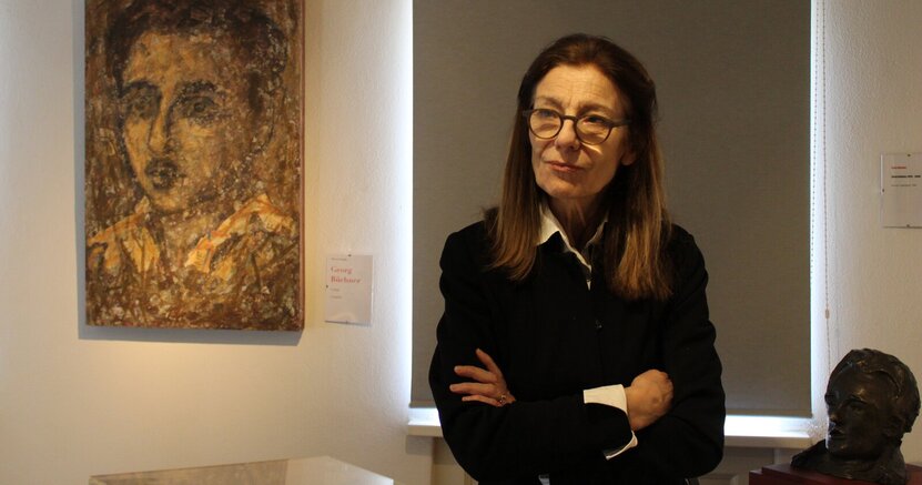 Ursula Krechel im Büchnerhaus. Ursula Krechel steht im Büchnerhaus zwischen einem Gemälde Georg Büchners und eine Büste von ihm.