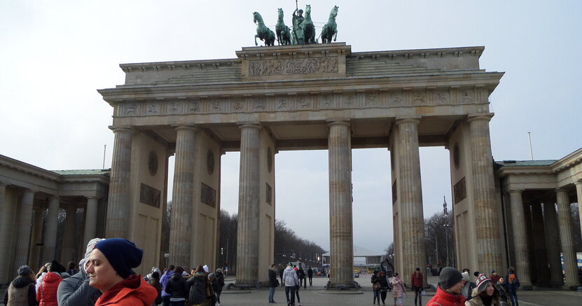 Auch das Brandenburger Tor gehört zu dem Besichtigungsprogramm der Berlinfahrt. Das Brandenburger Tor mit seinen hohen Säulen und der Figur der Wagenlenkerin und ihren Pferden oben auf dem Tor. Davor stehen Besucherinnen und Besucher.