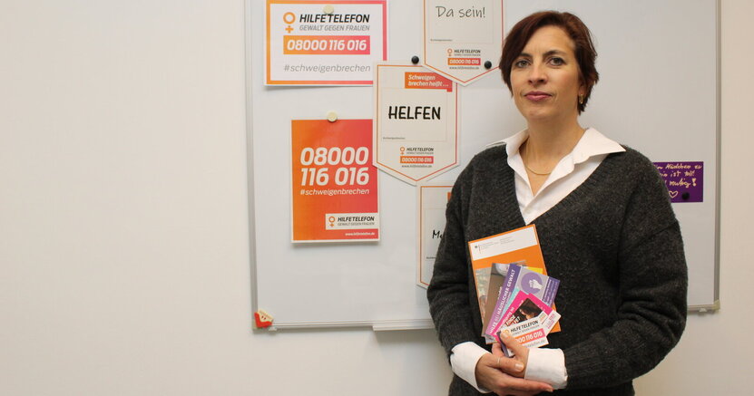 Die Riedstädter Frauen- und Gleichstellungsbeauftragte Jennifer Muth hat Infomaterial von Hilfeeinrichtungen zusammengestellt, das in den städtischen Kitas ausgelegt wird. Die Riedstädter Frauenbeauftragte Jennifer Muth steht vor einer Tafel mit Plakaten für das Hilfstelefon. In der Hand hält sie Broschüren mit weiteren Hilfsangeboten.