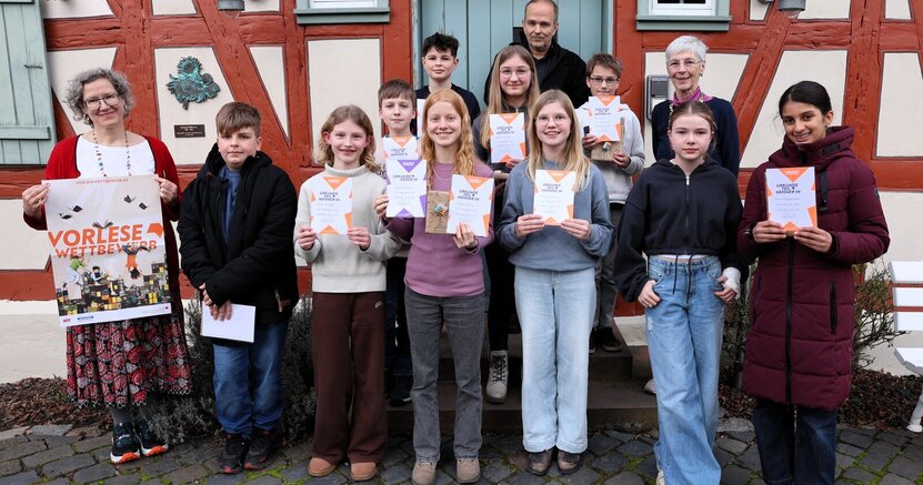 Gruppenbild des Vorlesewettbewerbs Groß-Gerau Süd vor dem Büchnerhaus mit den Juroren Lucia Bornhofen (li), Christian Suhr und Birgit Weinmann. Die Teilnehmerinnen und Teilnehmer des Vorlesewettbewerbs stehen vor dem Büchnerhaus. Mit dabei auch die Juroren Lucia Bornhofen (links), Christian Suhr und Birgit Weinmann. Die Kinder halten Teilnahmeurkunden in den Händen, Lucia Bornhofen ein Plakat mit der Aufschrift "Vorlesewettbewerb".