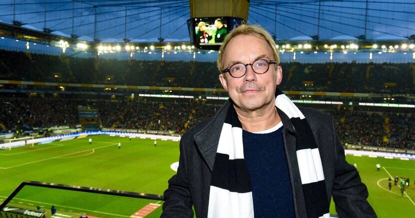 Henni Nachtsheim ist langjähriger Fan der Eintracht Frankfurt. Henni Nachtsheim steht mit schwarz-weißen Fan-Schal im Fußballstadion. Im Hintergrund ist das Spielfeld zu sehen.