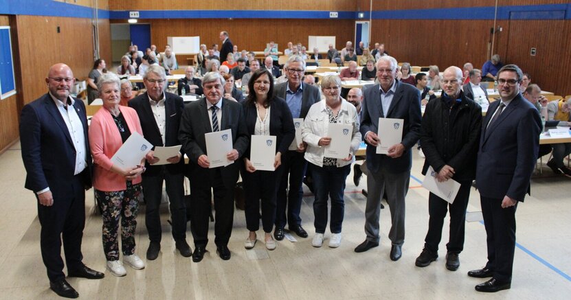 Bürgermeister Marcus Kretschmann (l.) und der wiedergewählte Stadtverordnetenvorsteher Guido Funk (r.) mit den neu gewählten Magistratsmitgliedern Monika Angelé, Klaus Knapp, Erster Stadtrat Richard Kraft, Melanie Dörr, Gerald Kummer, Carola Friedric Bürgermeister Marcus Kretschmann und Stadtverordnetenvorsteher Guido Funk stehen mit den neu gewählten Magistratsmitgliedern in einer langen Reihe in der Christoph-Bär-Halle. Die Magistratsmitglieder halten ihre Ernennungsurkunden in den Händen. Hinter ihnen sitzen die Stadtverordneten an ihren Tischen.