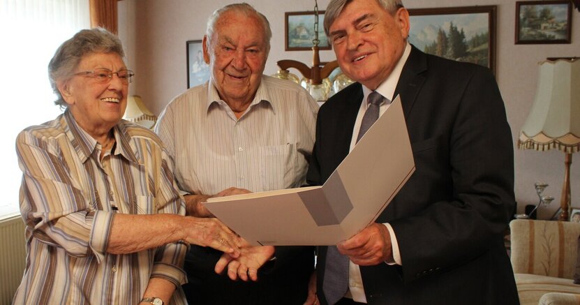 Dem Ehepaar Helga und Wilhelm Schneider überbrachte Erster Stadtrat Richard Kraft (v.li.) die herzlichsten Glückwünsche zur Eisernen Hochzeit Helga Schneider gibt lächelnd dem Ersten Stadtrat Richard Kraft die Hand. Dieser hält eine Mappe mit Glückwünsch-Urkunden in der Hand. Zwischen ihnen steht Wilhelm Schneider.