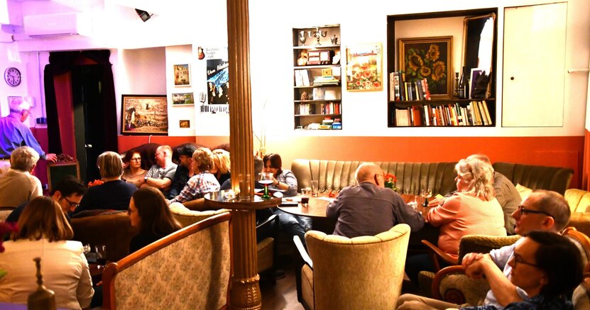 Im gemütlichen Theatercafé findet auch der Club der Dichter statt. Menschen sitzen in alten Sesseln im Theatercafé der BüchnerBühne.