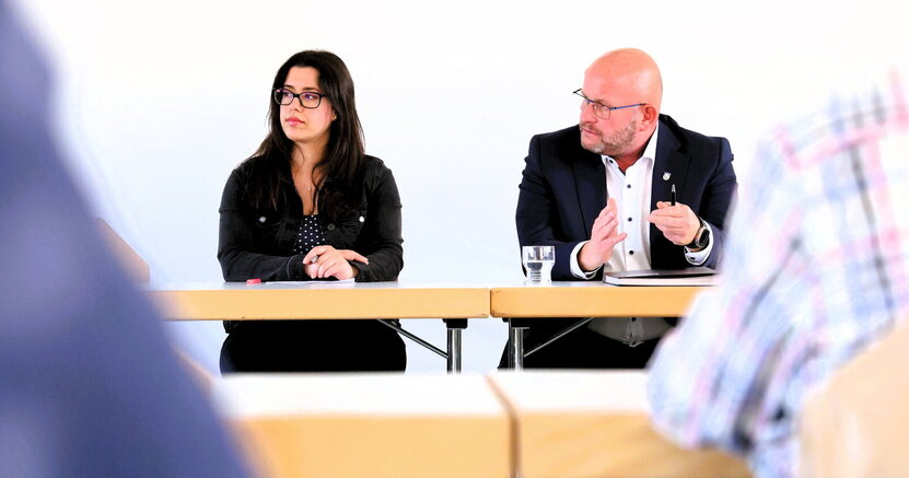 Bürgermeister Marcus Kretschmann mit Giulia Reinhardt vom Bürgerservice beim Bürgergespräch in Goddelau. Giulia Reinhardt vom Bürgerservice und Bürgermeister Marcus Kretschmann sitzen an einem Tisch, hinter ihnen befindet sich eine weiße Wand. Der Bürgermeister gestikuliert mit den Händen.