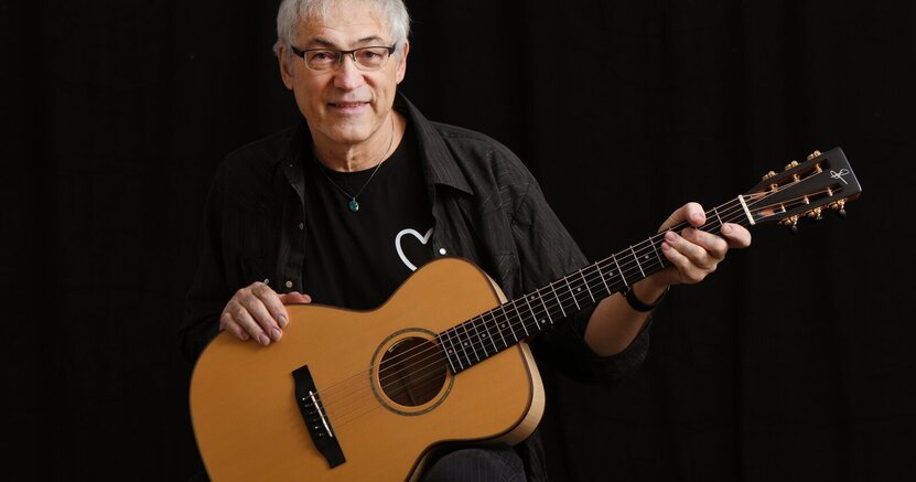 Don Alder kommt nach Riedstadt Don Alder trägt eine Brille und einen schwarzen Pullover, er hält seine Gitarre in der Hand. Der Hintergrund ist dunkel.