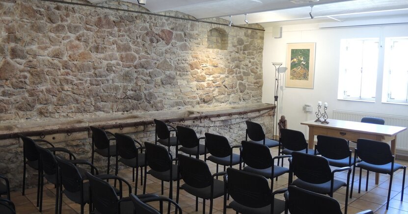 In der Kunstgalerie am Büchnerhaus wird das Theaterprojekt vorgestellt. In der Kunstgalerie am Büchnerhaus stehen Stuhlreihen vor einem Tisch. Die rückwärtige Längswand besteht aus großen alten Steinen.