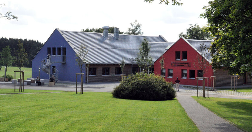 Zu sehen sind ein blaues und ein rotes Haus des Feriendorfs Ober-Seemen, im Vordergrund ist eine grüne Wiese.