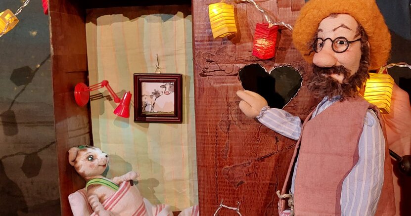 Ob das der neue Schlafplatz für Findus wird? Eine Handpuppe, die den Kater Findus darstellt, liegt mit Bettdecke und Kissen in einem Klohäuschen. Die Petersson-Puppe steht davor.