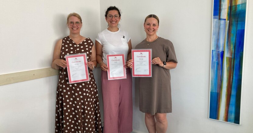 Die Erzieherinnen Anke Seibert, Hana Heil und Kristina Ligay mit ihren Zertifikaten Die Erzieherinnen Anke Seibert, Hana Heil und Kristina Ligay stehen in einem Sitzungsraum vor einer weißen Wand. Sie halten ihre Zertifikate in den Händen.