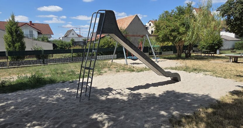 Auf dem Spielplatz Schulstraße wurde gemäß Spielplatzkonzept eine neue Rutsche aufgebaut. Auf dem Spielplatz Schulstraße steht eine neue Rutsche auf einem Sandfeld. Im Hintergrund ist noch eine Rasenfläche und dahinter Häuser zu sehen.