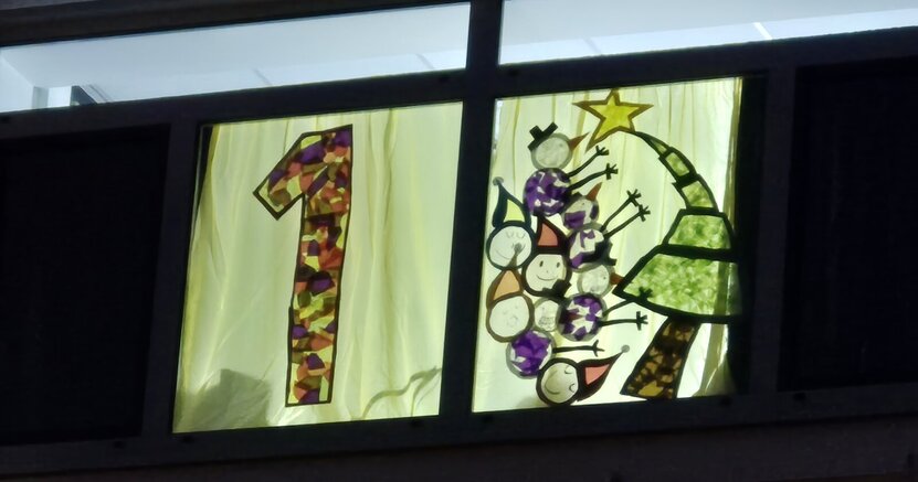 Das erste Adventsfenster erstrahlte am Abend des 1. Dezember. Im ersten Adventsfenster des Rathauses leuchtet eine bunte 1. Daneben ist ein Weihnachtsbaum mit Stern auf der Spitze zu sehen. Außerdem Schneemänner und Weihnachtswichtel.
